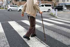 介護用品の杖を使って横断歩道を渡る老人